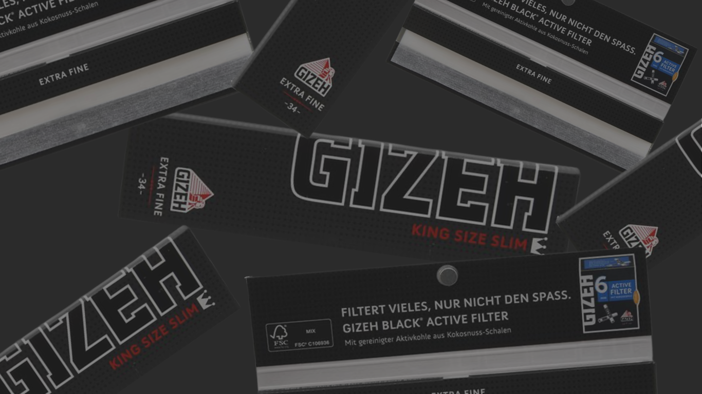 Banner mit GIZEH King Size Slim Longpapes und GIZEH Black Active Filter: schwarze Verpackungen mit großem „GIZEH“-Schriftzug, „King Size Slim“-Papers und „Extra Fine“-Hinweisen, dazu mehrere Filter-Packungen auf dunkelgrauem Hintergrund, teils schräg angeordnet und angeschnitten.