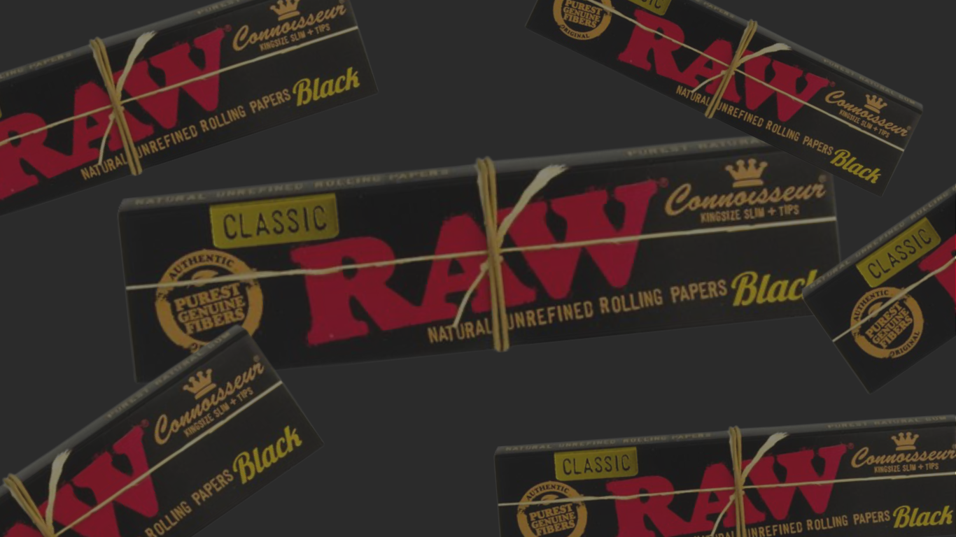 Banner mit RAW Black Classic Connoisseur King Size Slim Longpapes inkl. Tips: mehrere schwarze RAW-Packungen mit rotem Logo und goldenen Details auf dunkelgrauem Hintergrund, eine große Packung mittig, weitere schräg im Bild verteilt.
